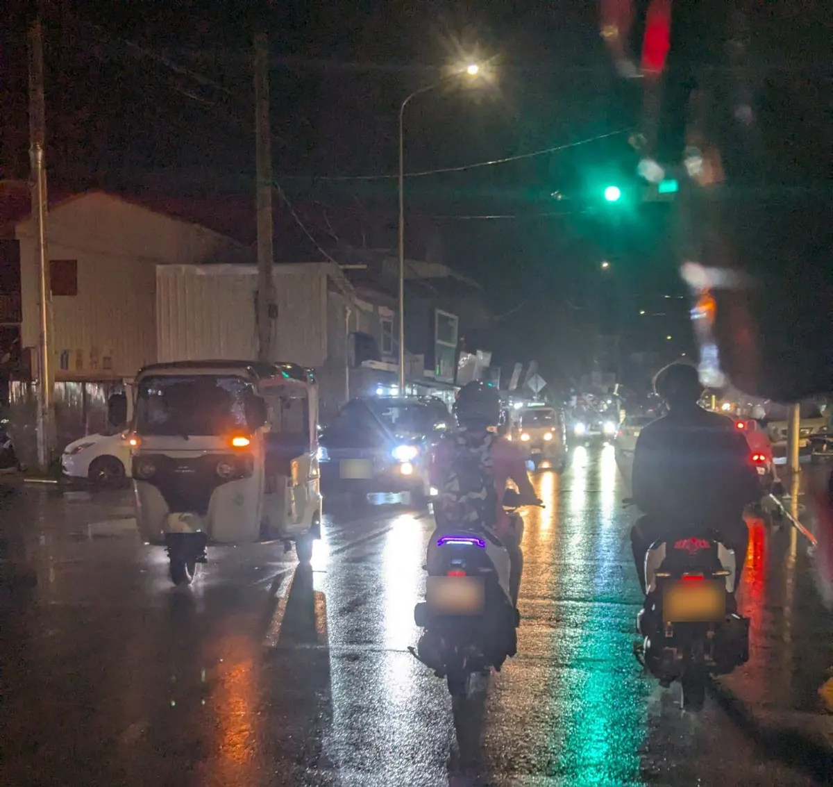Motorbikes and a tuk-tuk on a wet Siem Reap street at night after the rain